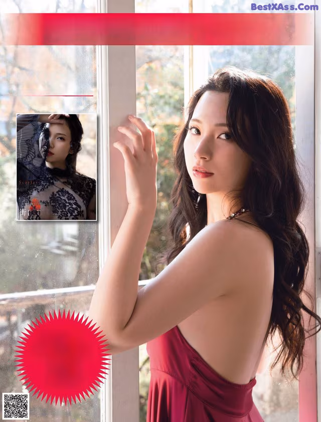 A woman in a red dress standing by a window.