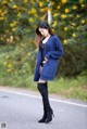 A woman in a blue coat is standing on the side of the road.