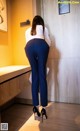 A woman in a white shirt and blue pants leaning against a wall.