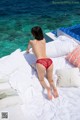 A woman in a red bikini laying on a bed by the ocean.