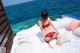 A woman in a red lingerie sitting on a bed by the ocean.