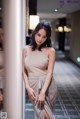 A woman in a beige dress leaning against a wall.