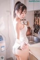 A woman in a white dress standing in a kitchen.