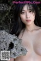 A naked asian woman posing in front of a rock.