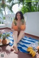 A woman sitting on a towel holding two pineapples.