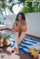 A woman sitting on a towel holding two pineapples.