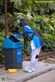 A woman in a blue and white outfit standing next to a trash can.