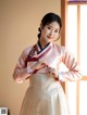 A woman in a pink and white hanbok is posing for a picture.