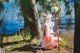 A woman in a pink dress holding a staff in front of a lake.