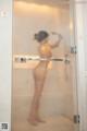 A naked woman standing in a glass shower door.