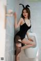 A woman in a black dress sitting on a toilet.