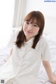 A woman sitting on a bed wearing a white shirt.