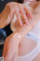 A woman in a white tank top is applying cream on her arm.