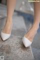 A close up of a woman's legs wearing white shoes.