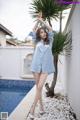 A woman in a blue shirt and white shoes posing by a pool.