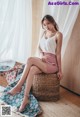 A woman sitting on top of a wicker chair next to a window.