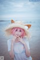 A woman with pink hair wearing a straw hat on the beach.