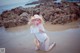 A woman in a white dress and a straw hat on a beach.