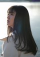 A woman with long black hair standing by the water.