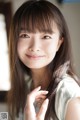 A young woman with long brown hair and bangs smiles at the camera.