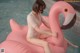 A woman sitting on an inflatable flamingo in a pool.